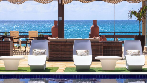 Un espace aménagé au bord de la piscine, avec des chaises longues et une vue sur l’océan.