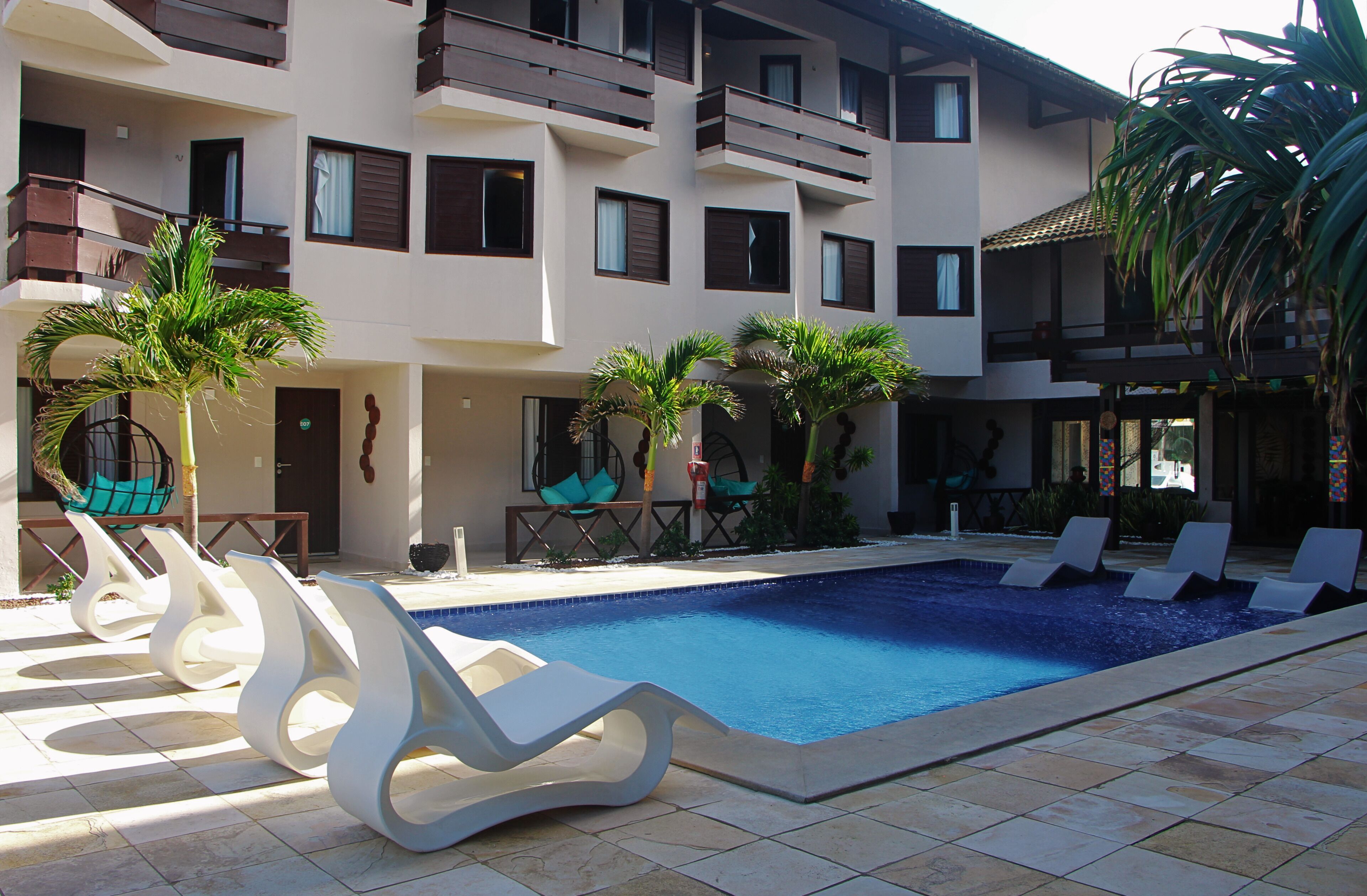 Una piscina con sillas de descanso, palmeras y un edificio de varios pisos con balcones.