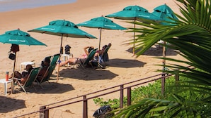 Une plage avec des parasols verts et des chaises, un rivage sablonneux et l’océan.