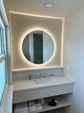A bathroom with a round mirror, a white sink, and a towel rack.
