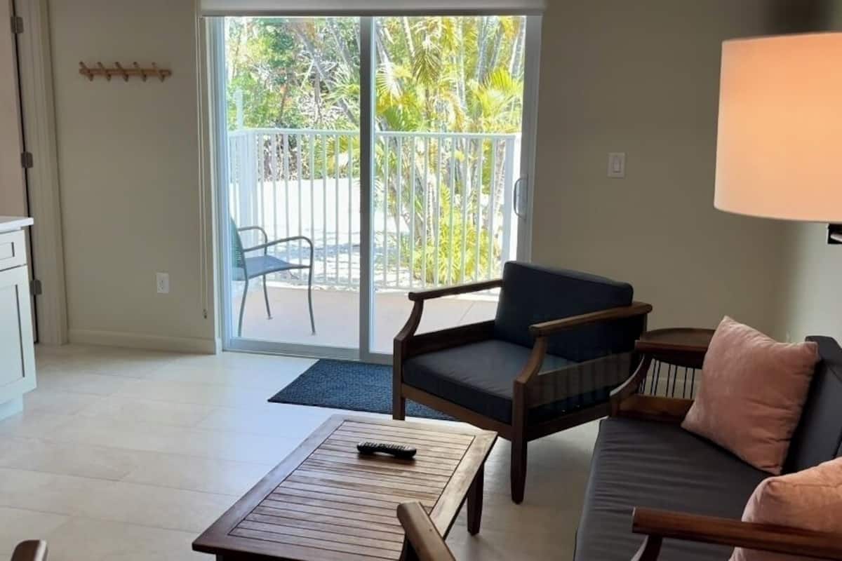 A living room with a sofa, armchairs, a coffee table, and a sliding glass door leading to a balcony.