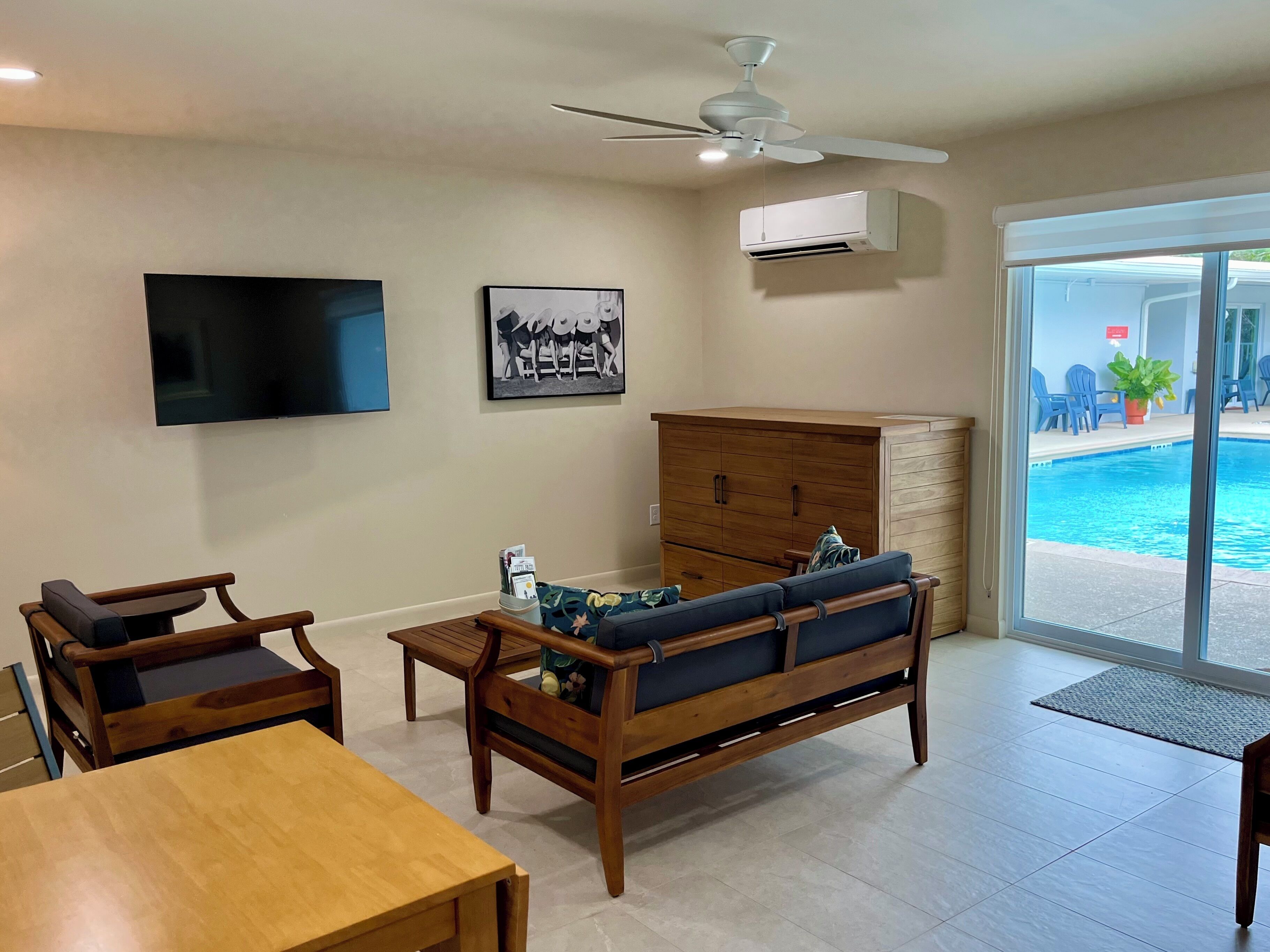 Una sala de estar con televisor, ventilador de techo, sofá y un mueble de madera.