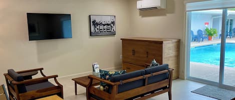 Una sala de estar con televisor, ventilador de techo, sofá y un mueble de madera.