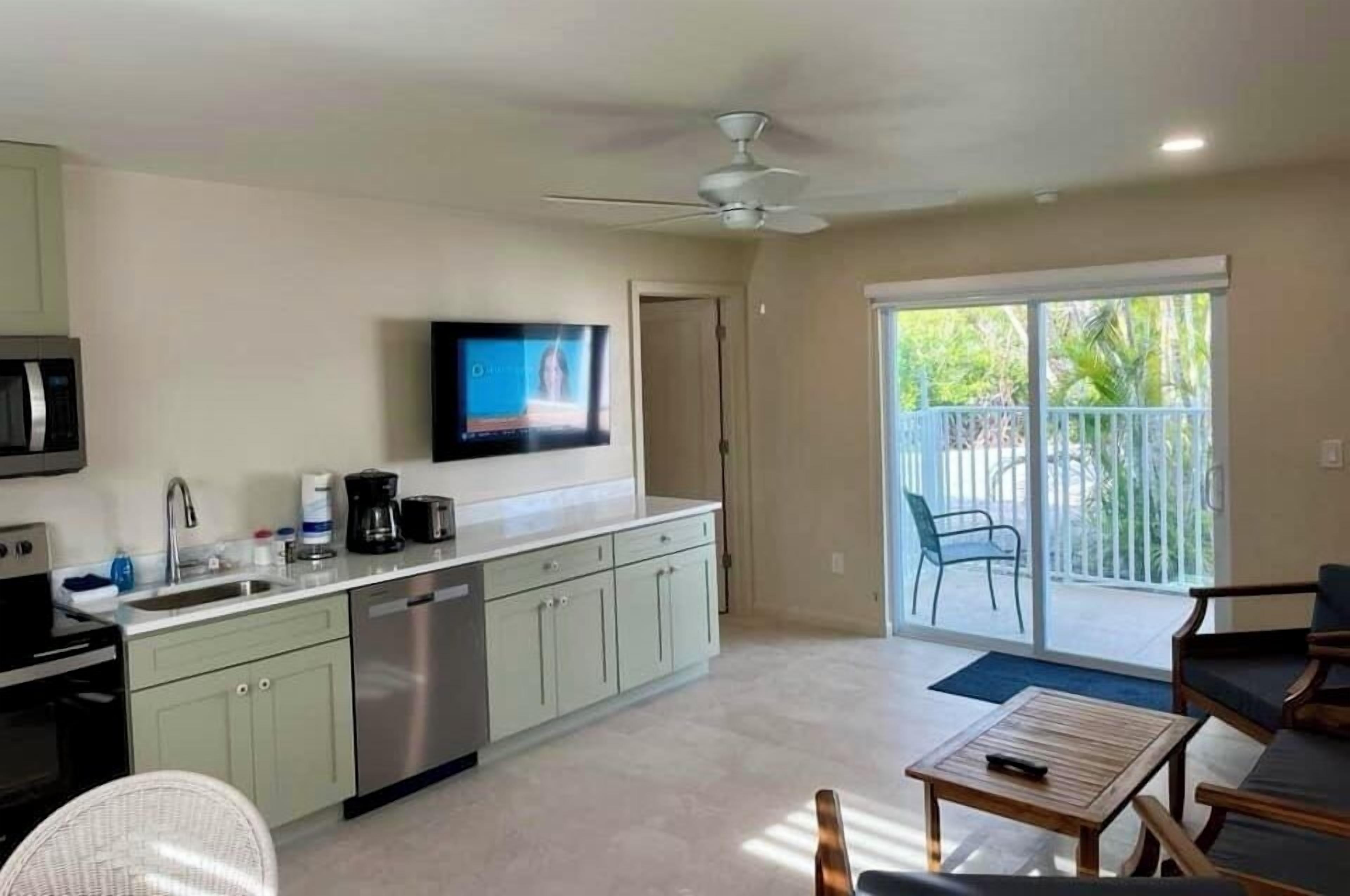 A modern kitchen with a flat-screen TV, a ceiling fan, and a sliding glass door leading to a balcony.