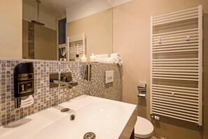 Un baño moderno con un lavamanos grande, un inodoro, un lava manos y un espejo con un perchero para toallas.