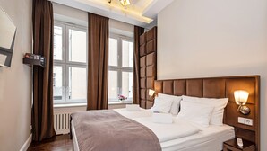 Ein Hotelzimmer mit einem großen Bett, einem Nachttisch mit Lampe, einem Fenster mit Vorhängen und einer Heizung.