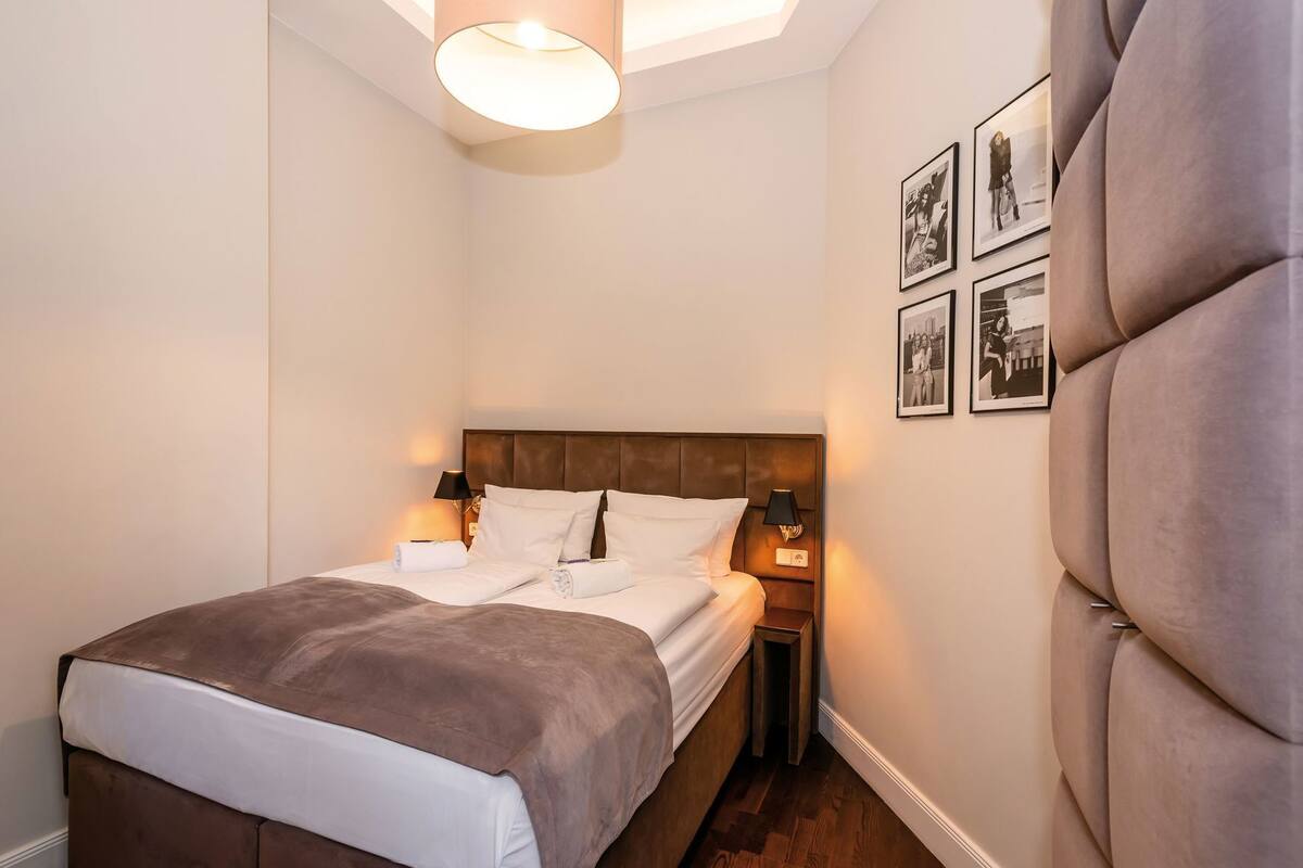 Una habitación de hotel con cama, lámparas de noche, mesita de noche y un muro con cuadros.