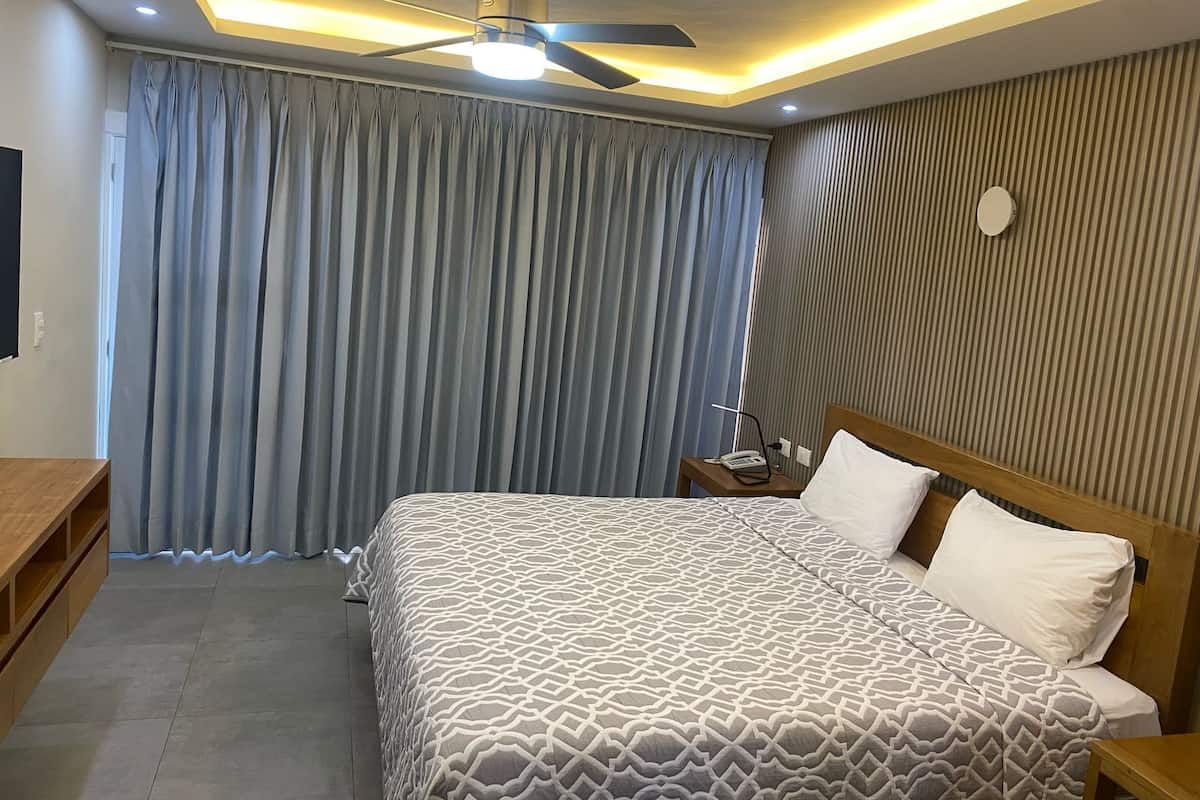 A hotel room with a bed, a desk, a ceiling fan, and a nightstand with a phone and lamp.