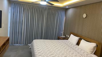 A hotel room with a bed, a desk, a ceiling fan, and a nightstand with a phone and lamp.