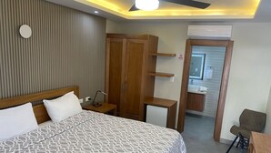 A modern hotel room with a large bed, wooden wardrobe, bedside table, and a small desk with a chair. - New Garden Hotel (Sosúa)