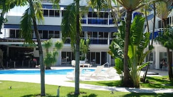 Un hotel con piscina, sillas de descanso y palmeras.
