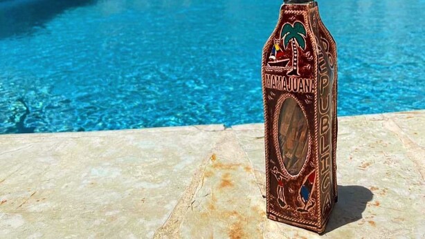 Een fles Margaritaville Rum bij een zwembad, met een helderblauw zwembad en palmbomen op de achtergrond.
