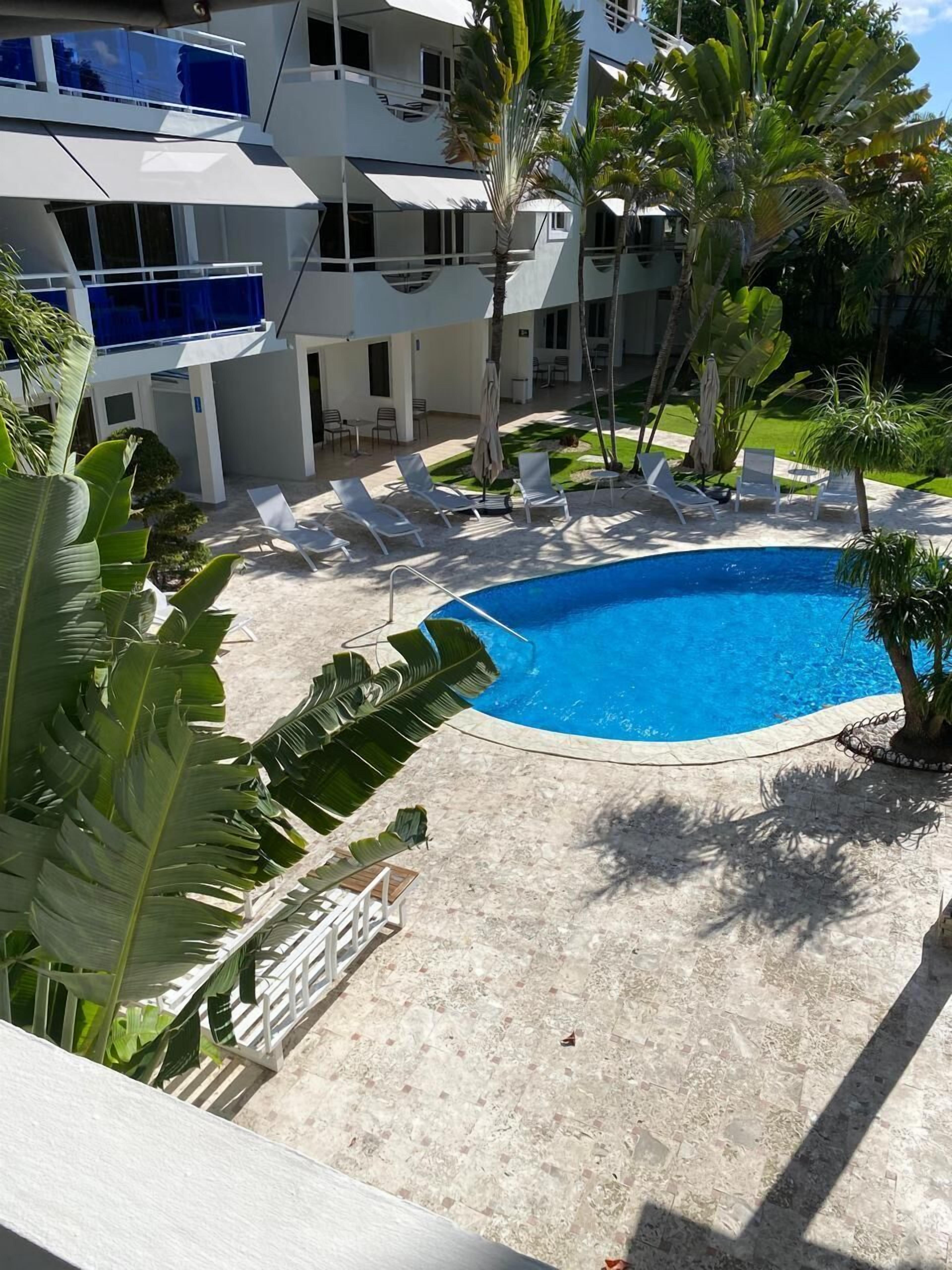 Una piscina circondata da lettini, palme e un edificio moderno con balconi.