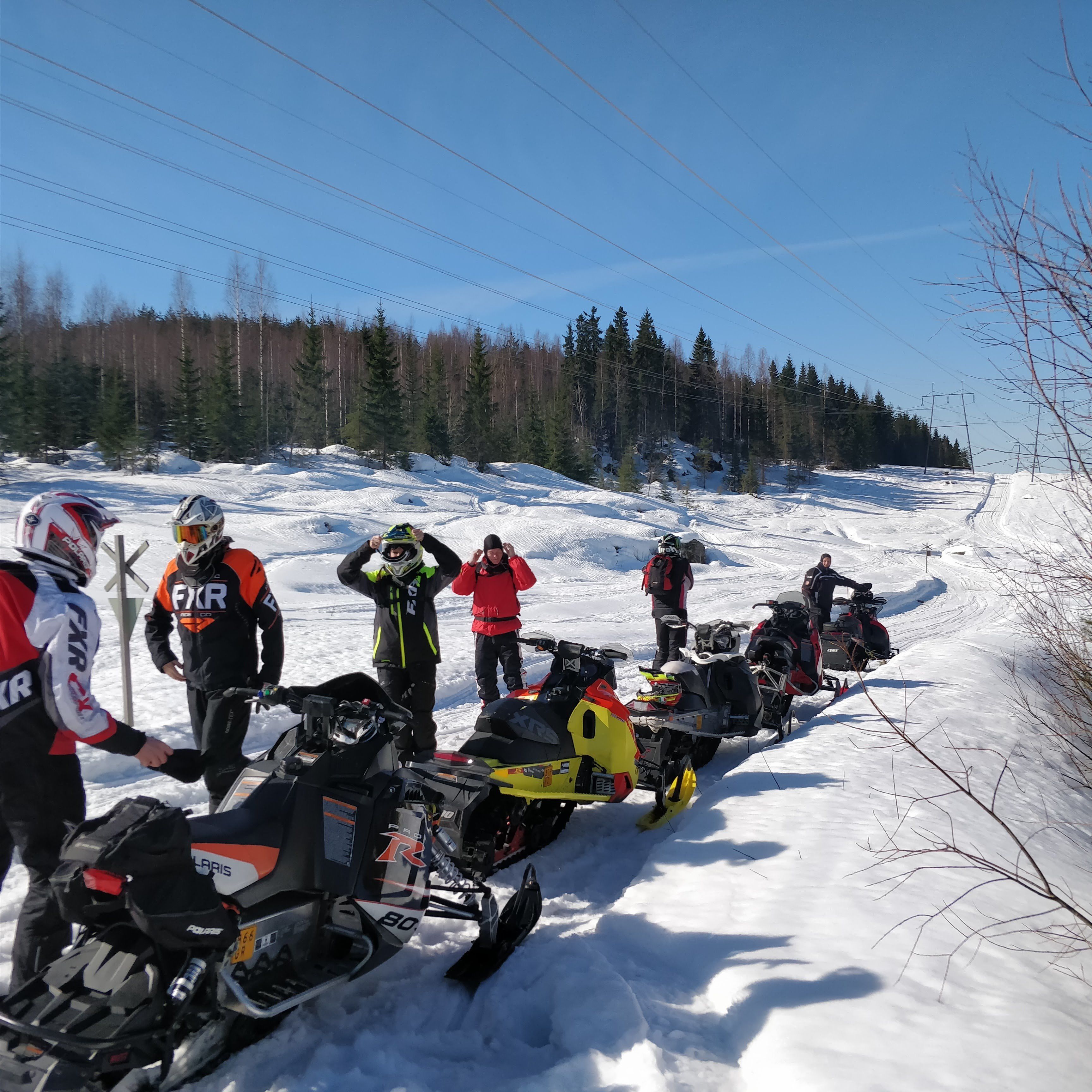 A group of snowmobiles lined up on a snowy path with trees in the background.
