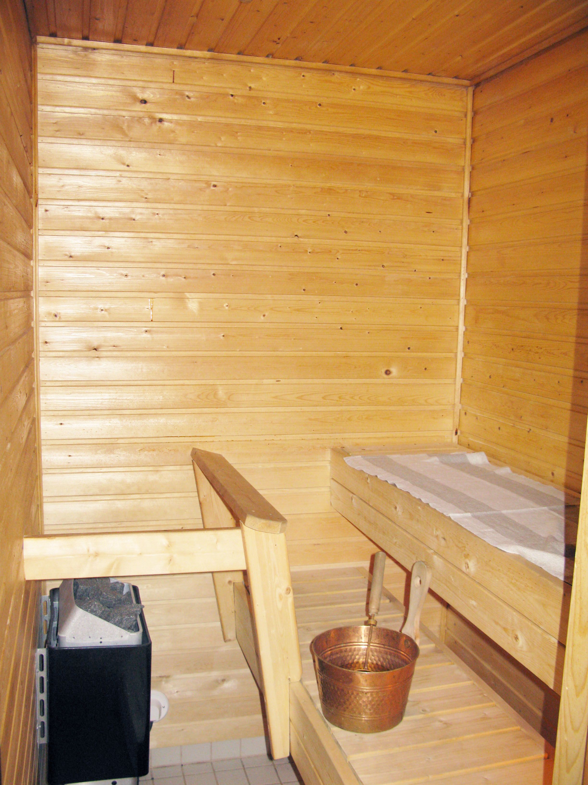A wooden sauna with a bench, a bucket, and a small black trash bin.