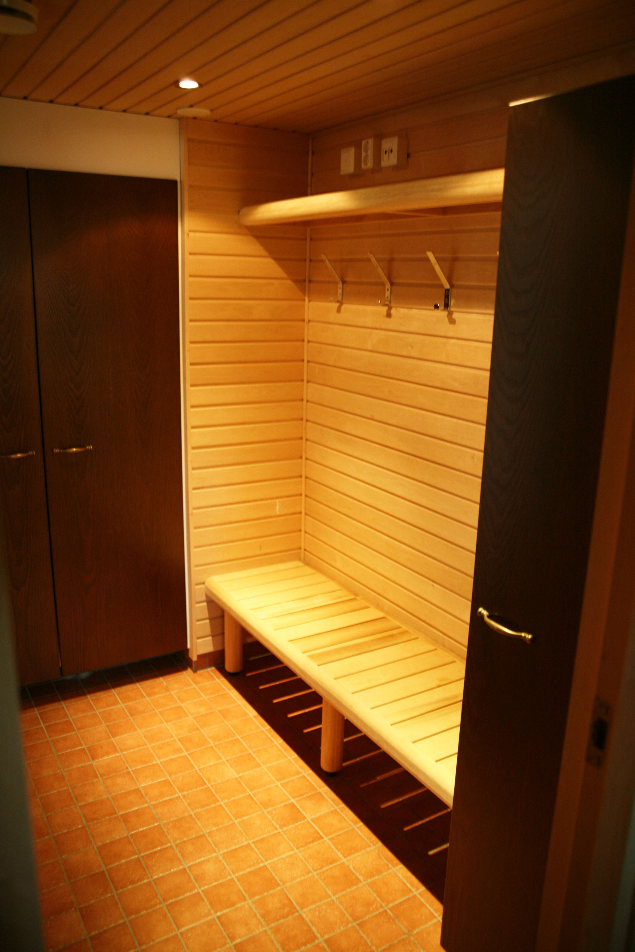 Un pequeño sauna con techo bajo, una banca, paredes de madera y suelo de baldosas.