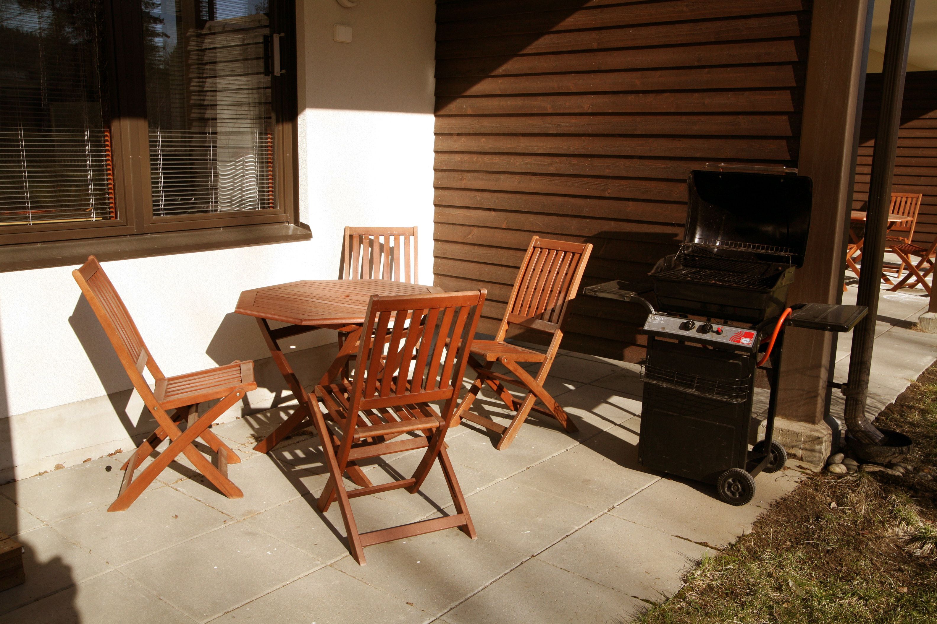 Un patio al aire libre con una mesa, sillas, una parrilla y una ventana con persianas.