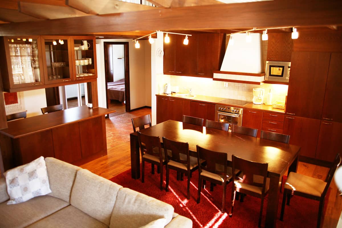 A spacious living area with a sofa, a dining table with chairs, a kitchen with wooden cabinets, and a red carpet.