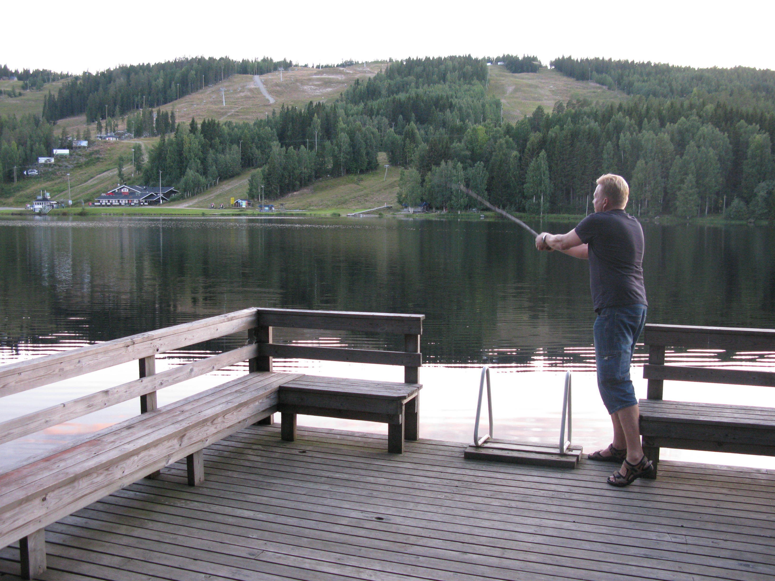 A wooden dock with benches overlooking a calm lake, surrounded by forested hills.
