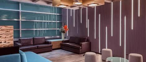 A modern lobby with a sectional sofa, round ottomans, a glass coffee table, and a wooden accent wall.