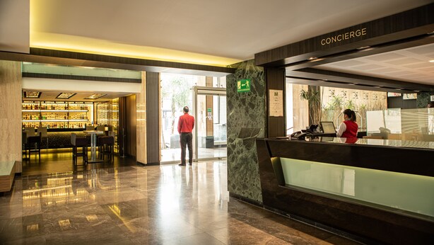 Un vestíbulo de hotel con una recepción, una zona de bar y un espacio para sentarse.