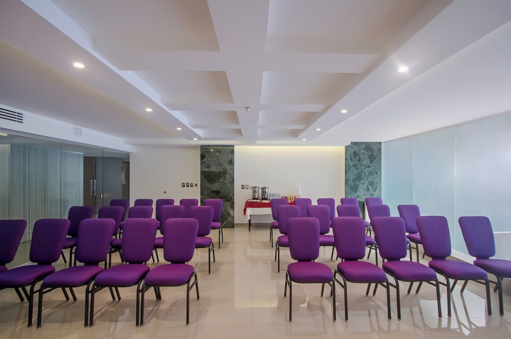 A conference room with rows of purple chairs, a marble wall, and a red table with a white cloth.