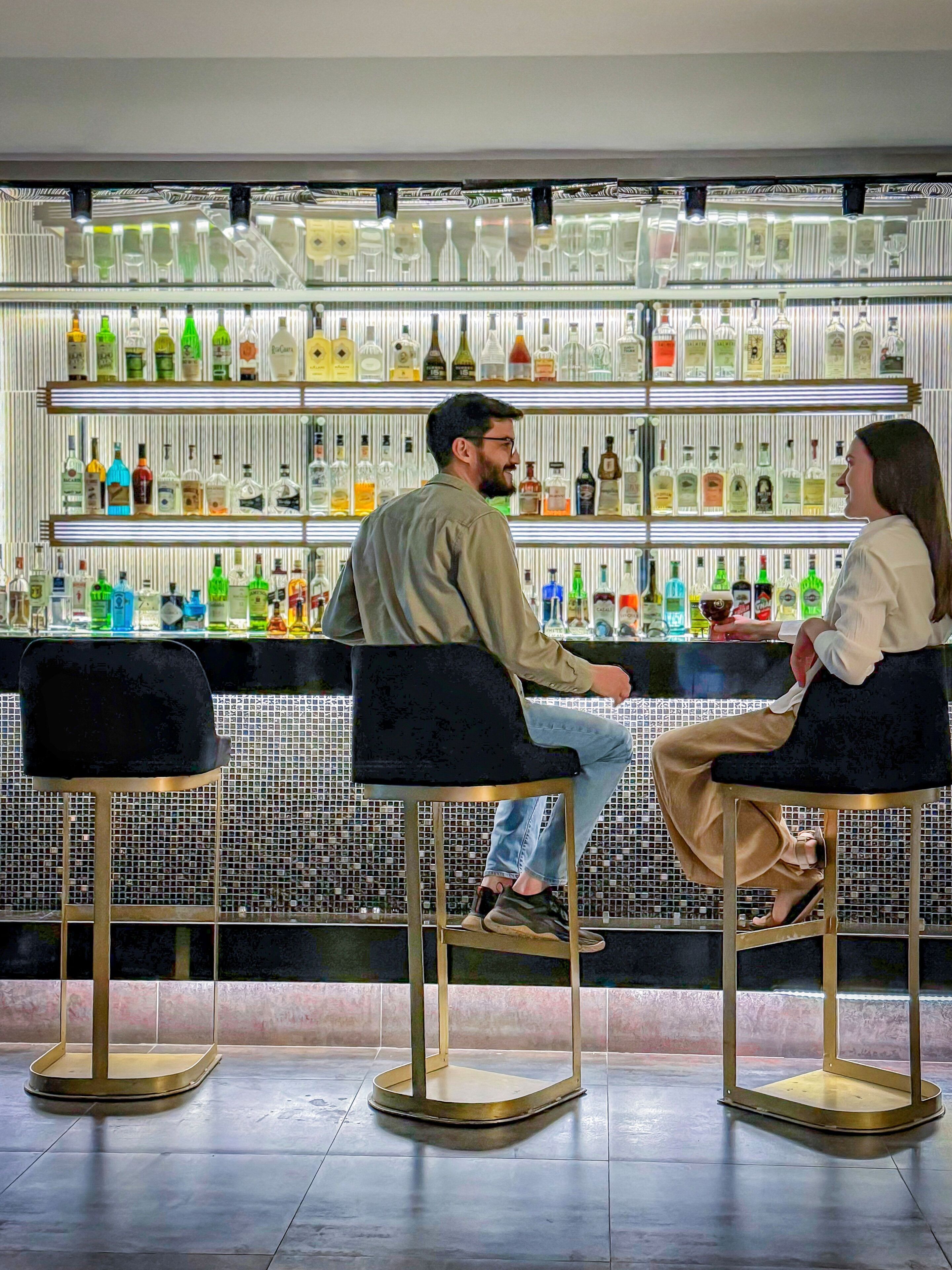 A bar area with two stools and a shelf of liquor bottles.