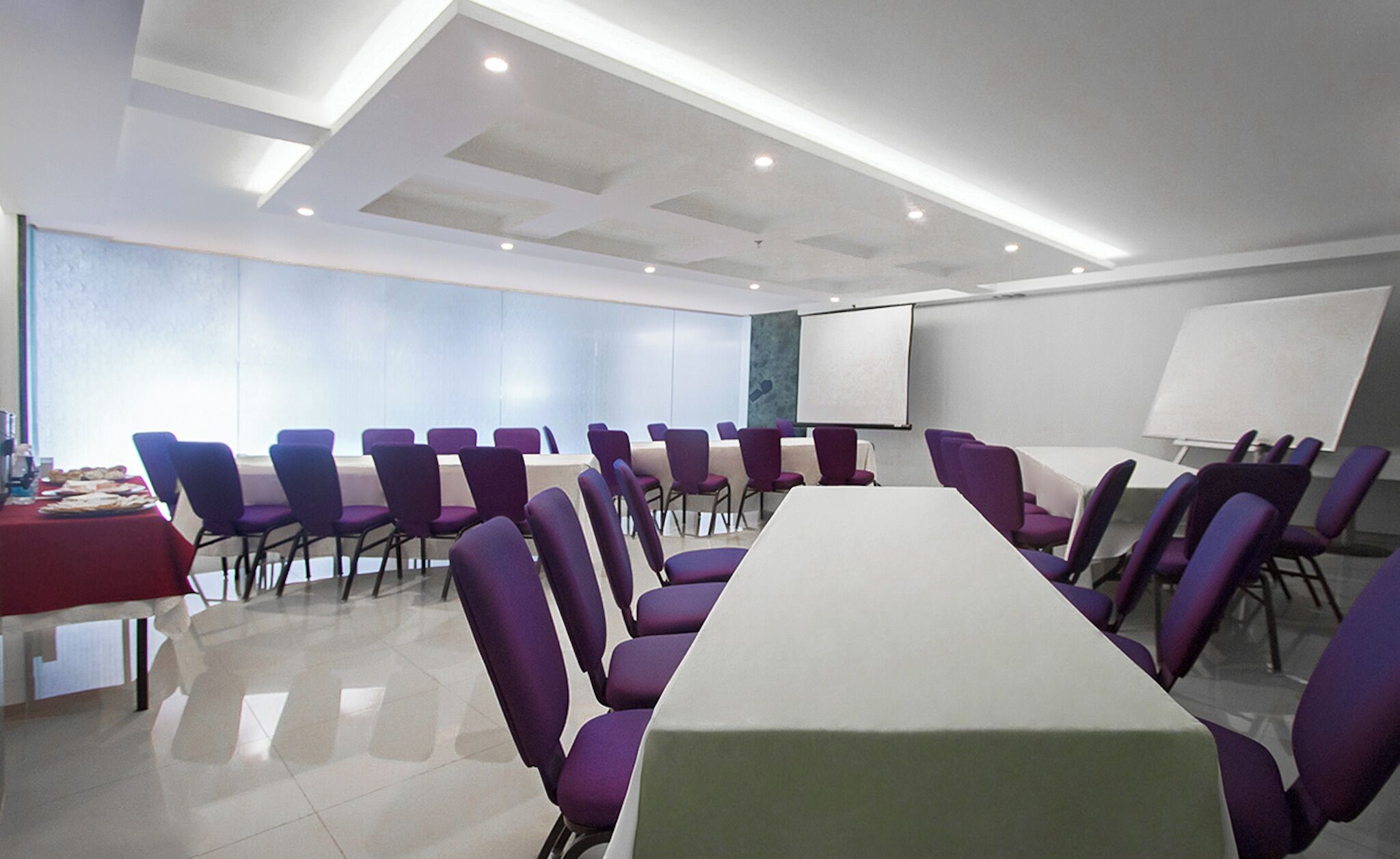 A conference room with a long table, purple chairs, a whiteboard, and a projector screen.