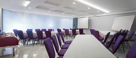 A conference room with a long table, purple chairs, a whiteboard, and a projector screen.