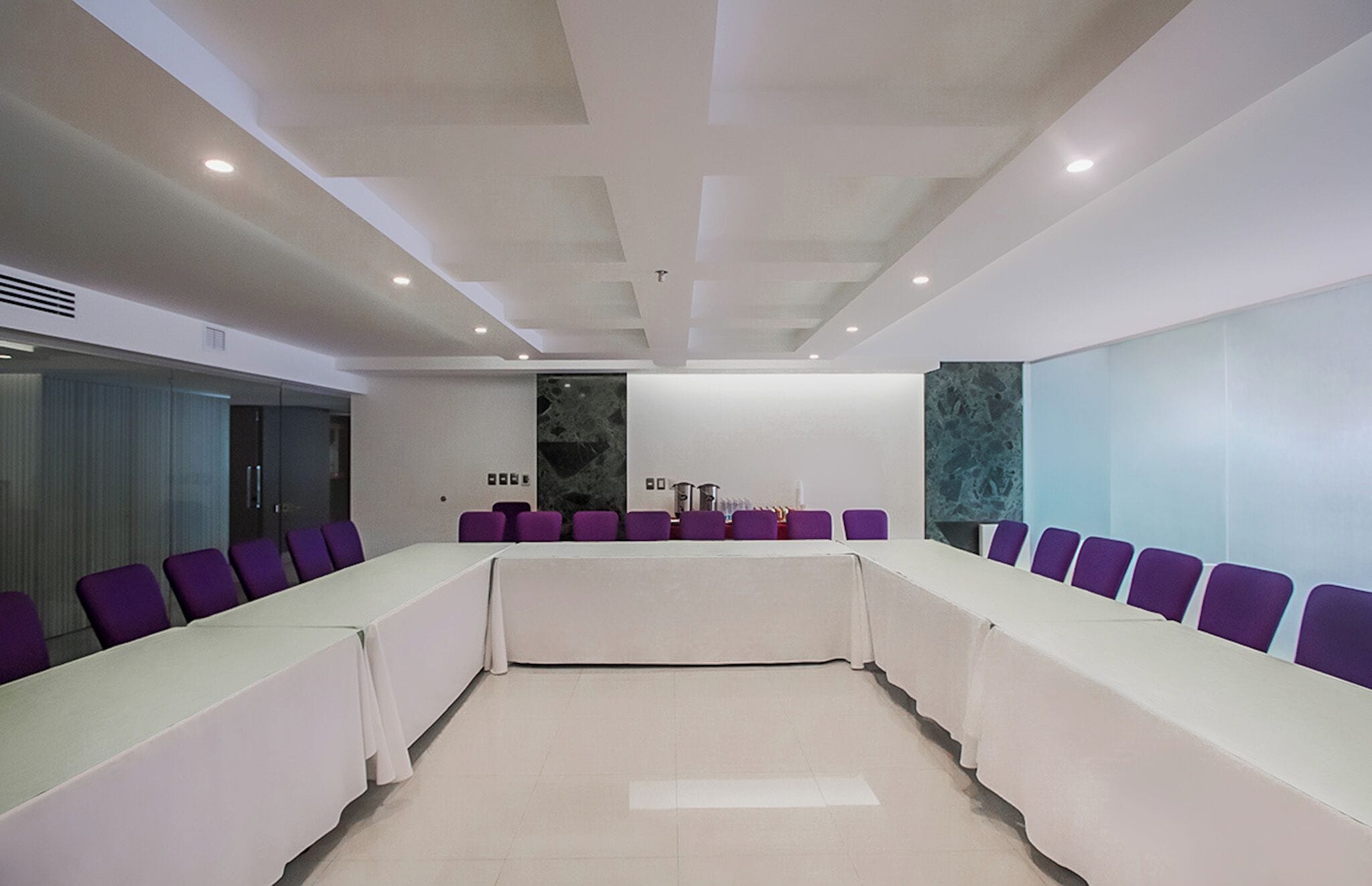 Ein Konferenzraum mit einem langen Tisch, violetten Stühlen und einem modernen Deckenstil.