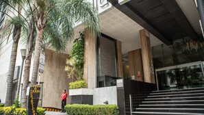 Entrada moderna de un edificio con un cartel que dice 'SITIO D TURISTICOS' y un guardia de seguridad.