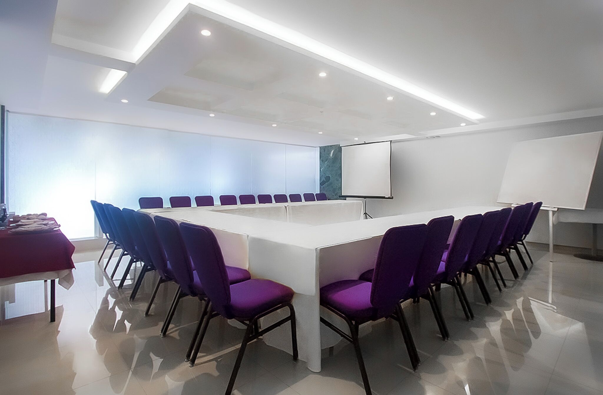 Une salle de conférence avec une longue table, des chaises violettes, un tableau blanc et un écran de projection.