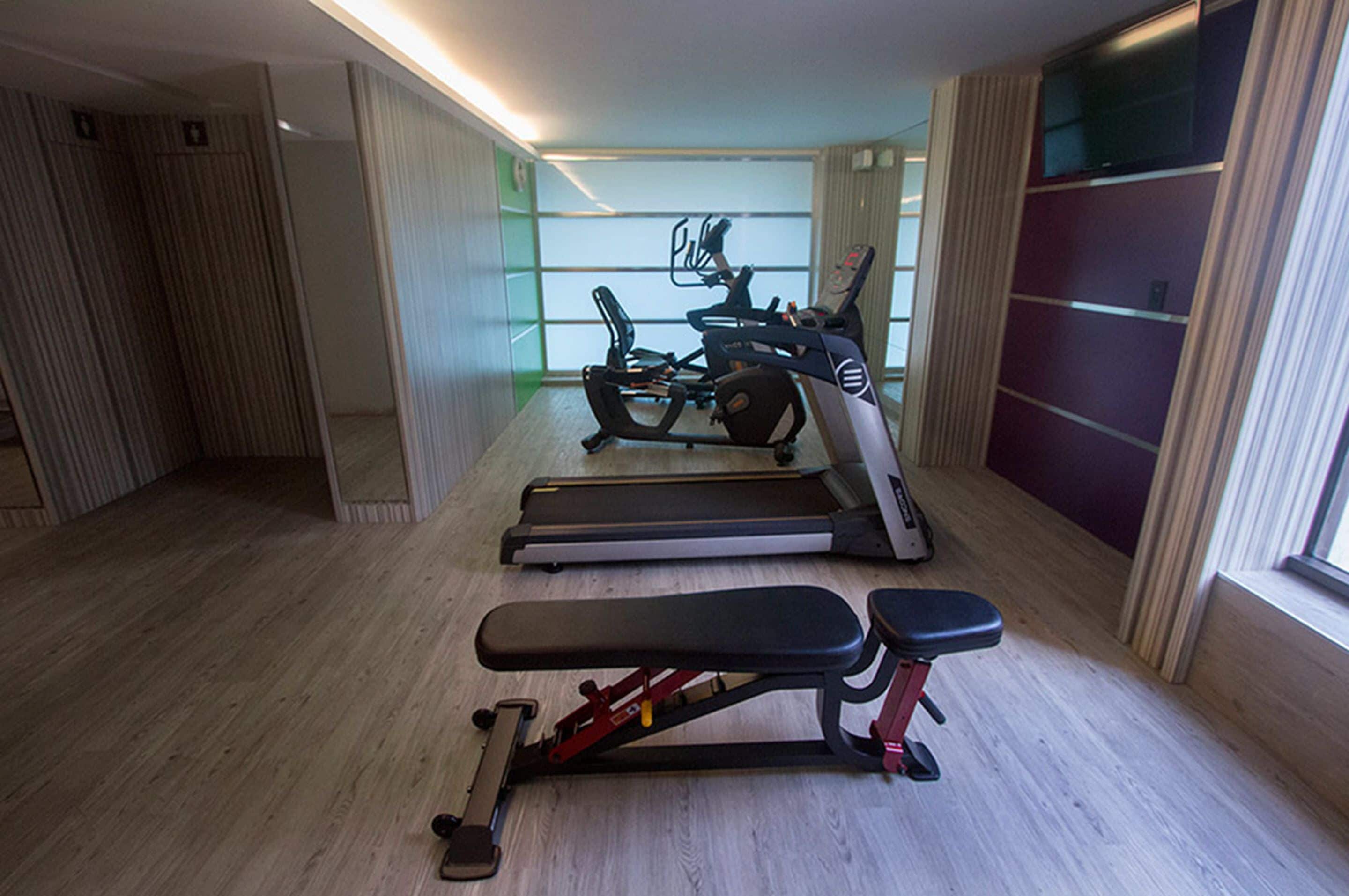 Une salle de sport équipée de matériel d’exercice, notamment des tapis de course et un banc de musculation.