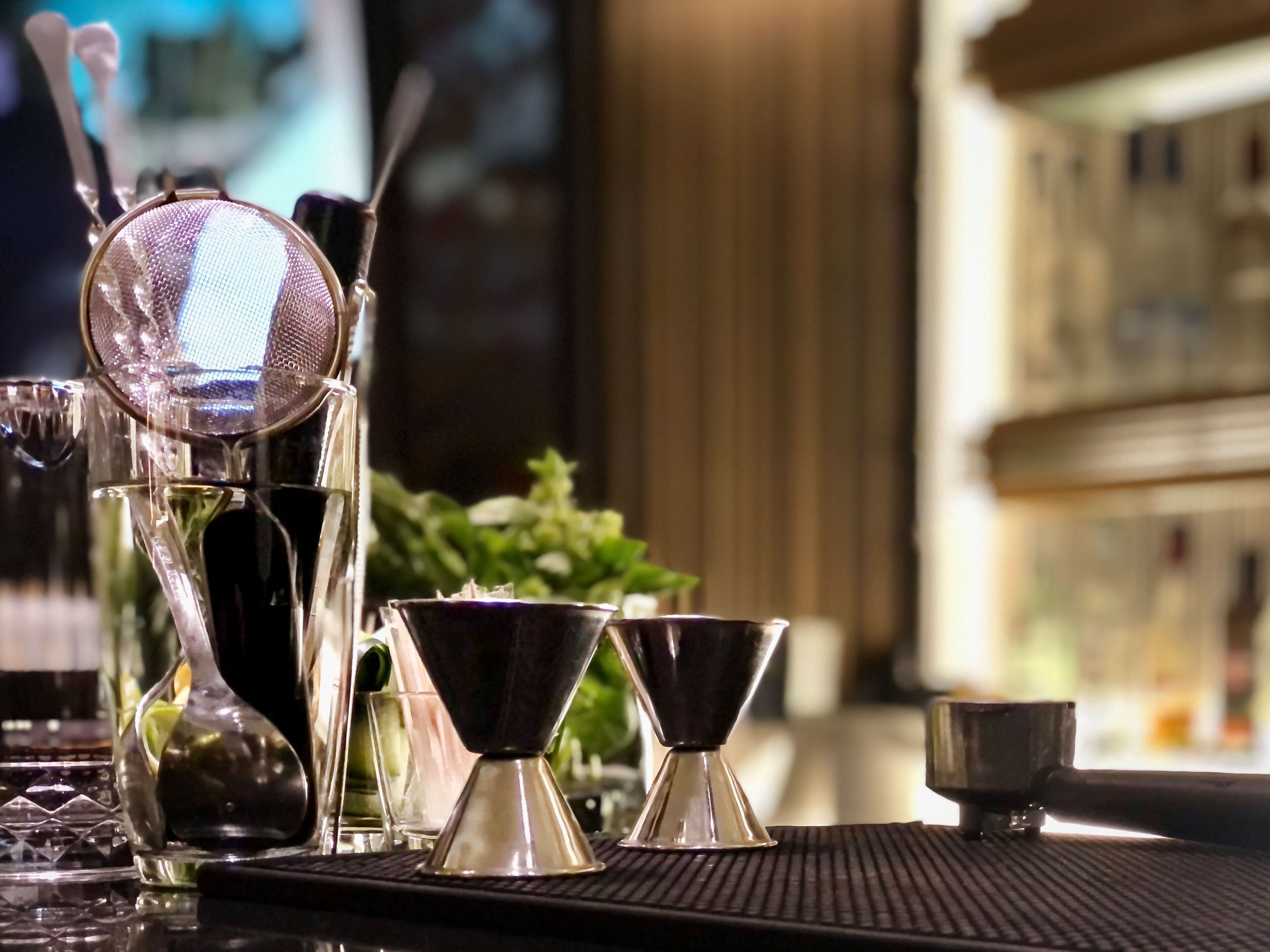 Un bar con diferentes vasos, incluyendo un colador, un medidor y una coctelera.
