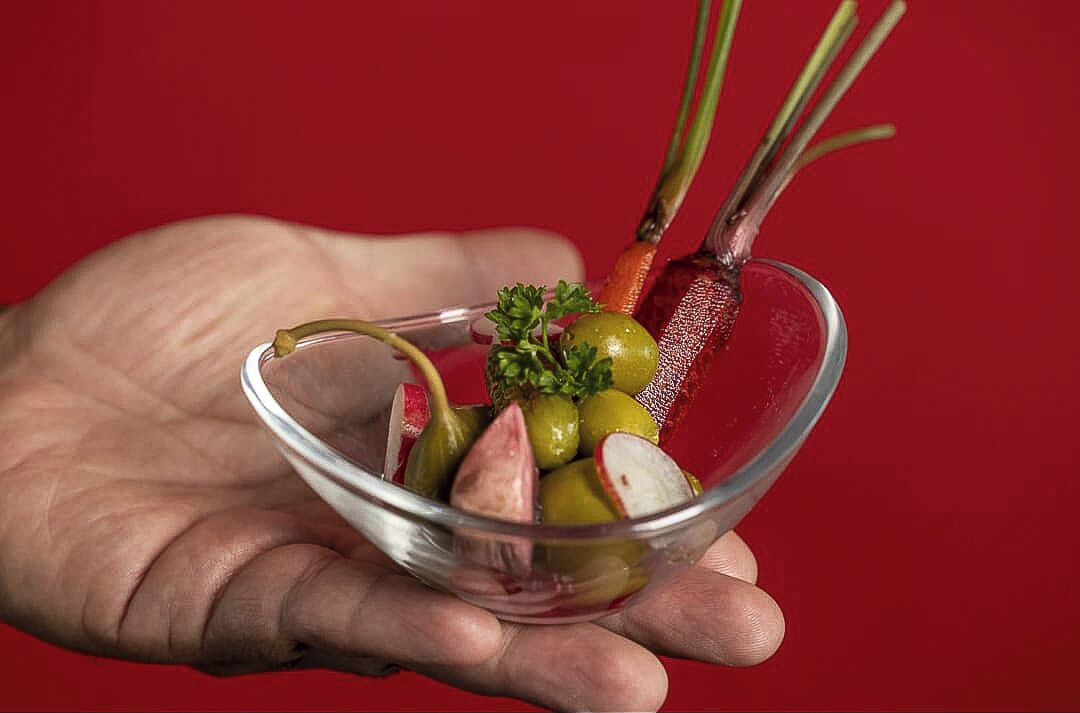 Une main tenant un bol en verre transparent rempli de légumes coupés en tranches.
