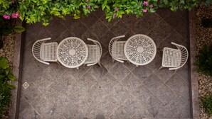 Un patio con cuatro sillas blancas y una mesa, alineados en un piso de baldosas.