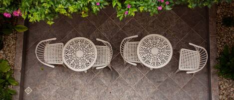 A patio with four white chairs and a table, arranged in a row on a tiled floor.