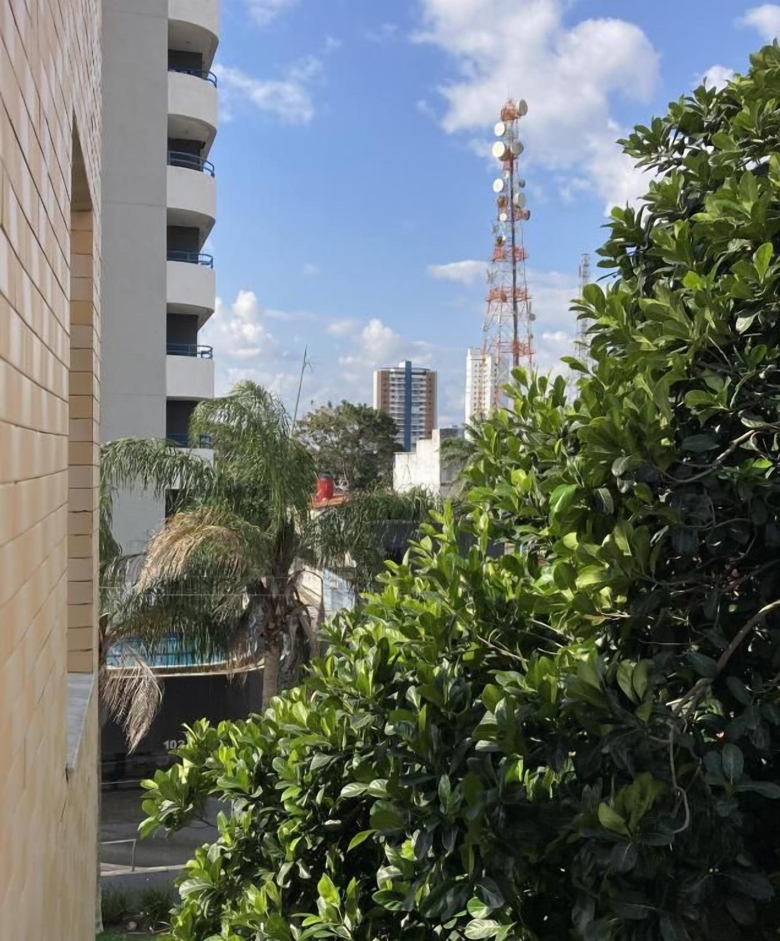 Un edificio de varios pisos, rodeado de vegetación y un cielo despejado.