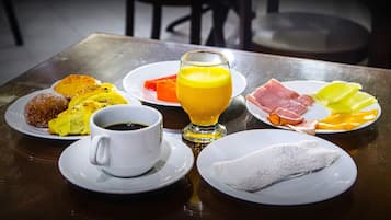 Uma mesa posta para o café da manhã, com pratos de comida, um copo de suco de laranja e uma xícara de café.