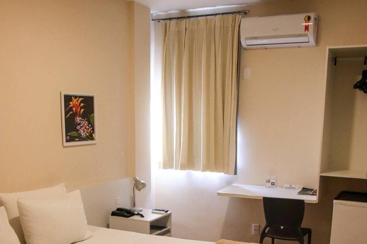 Habitación de hotel con una cama grande, un escritorio, una silla, un refrigerador pequeño y un equipo de aire acondicionado.