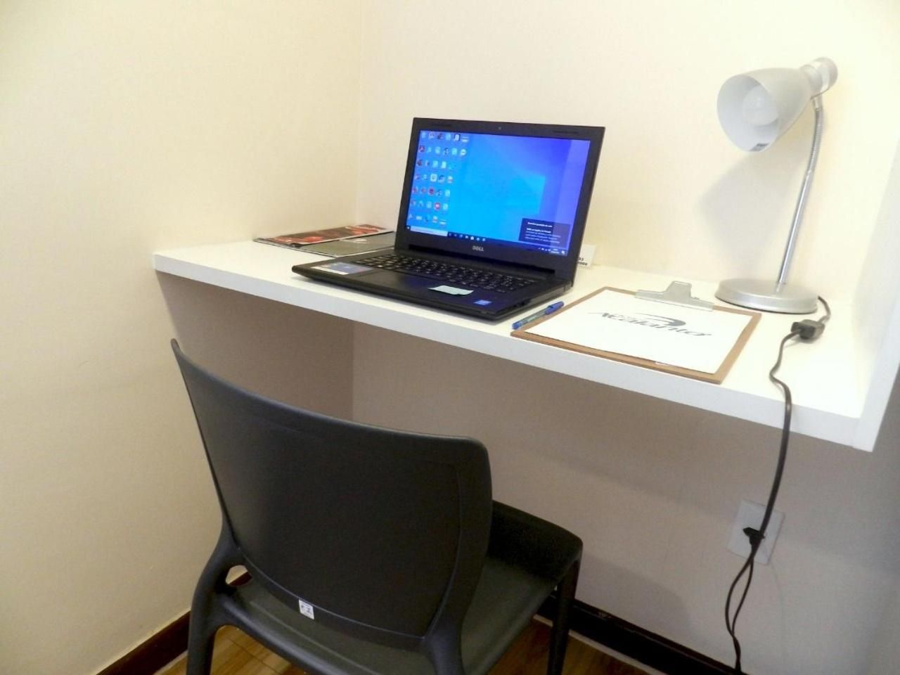 A laptop on a desk with a chair in front, a lamp, and a sign on the wall.