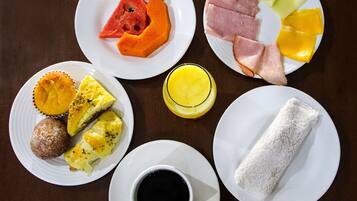 A breakfast table with plates of food, including eggs, ham, fruit, and a cup of coffee.