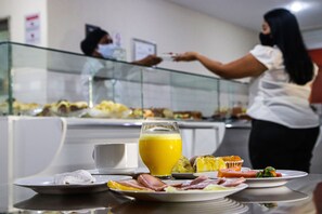 Un bufé de desayuno con diversos platos y un vaso de zumo de naranja en una mesa.