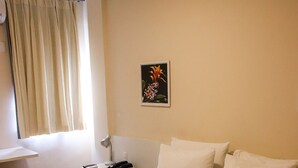Habitación de hotel con una cama grande, una mesita de noche con lámpara, una pequeña mesa y una ventana con cortinas.