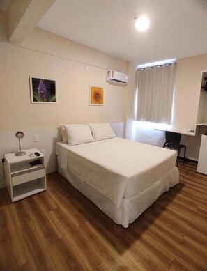 Une chambre à coucher avec un lit, une table de chevet, un bureau et une fenêtre avec des rideaux.