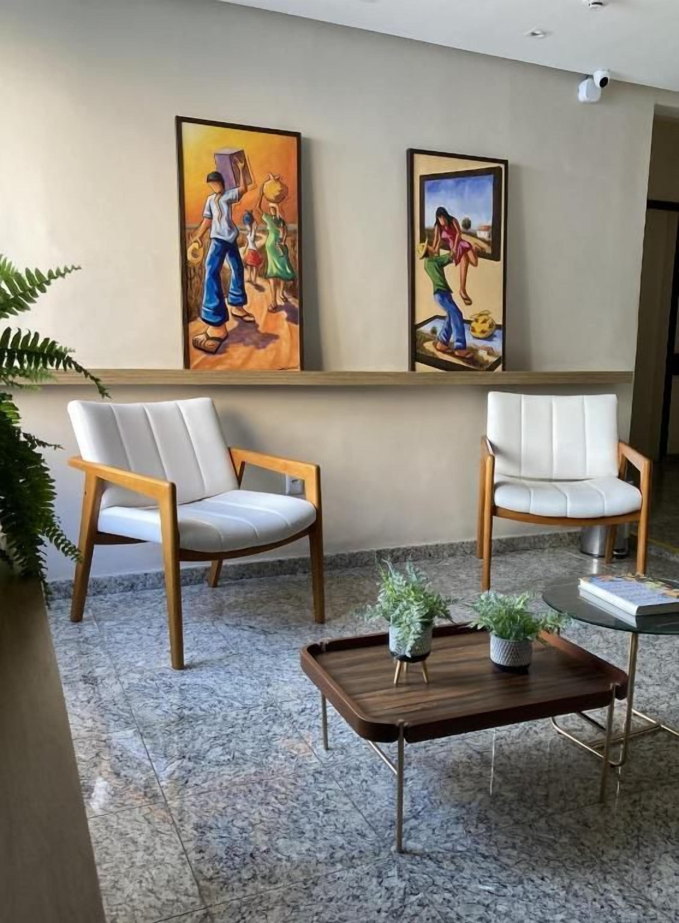 A room with two chairs, a small table with a plant, and two framed artworks on the wall.