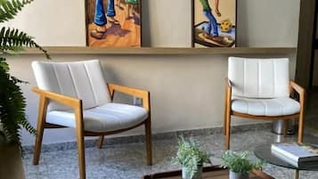 Una habitación con dos sillones, una mesita con una planta y dos cuadros enmarcados en la pared.