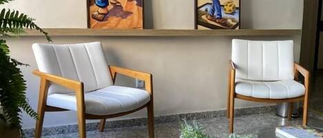 A room with two chairs, a small table with a plant, and two framed artworks on the wall.