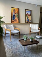 A room with two chairs, a small table with a plant, and two framed artworks on the wall.