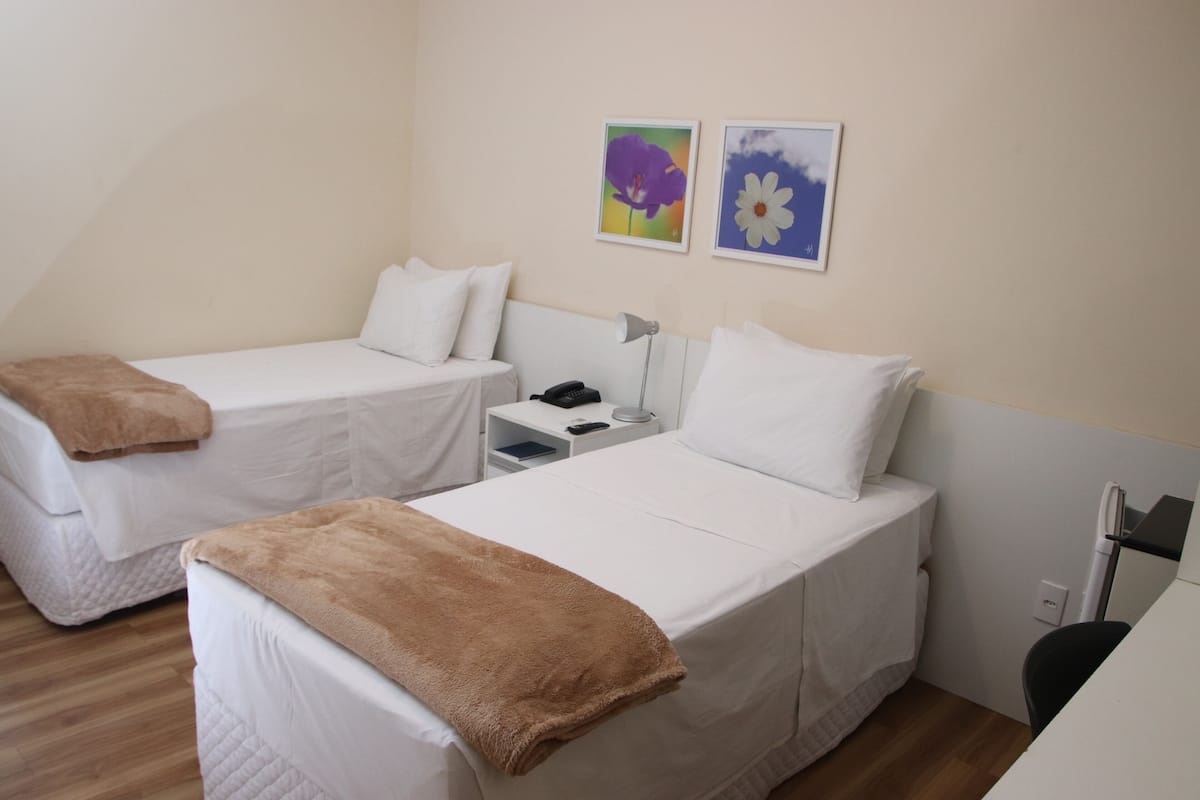 Una habitación con dos camas individuales, una mesita de noche con lámpara y dos cuadros enmarcados en la pared.